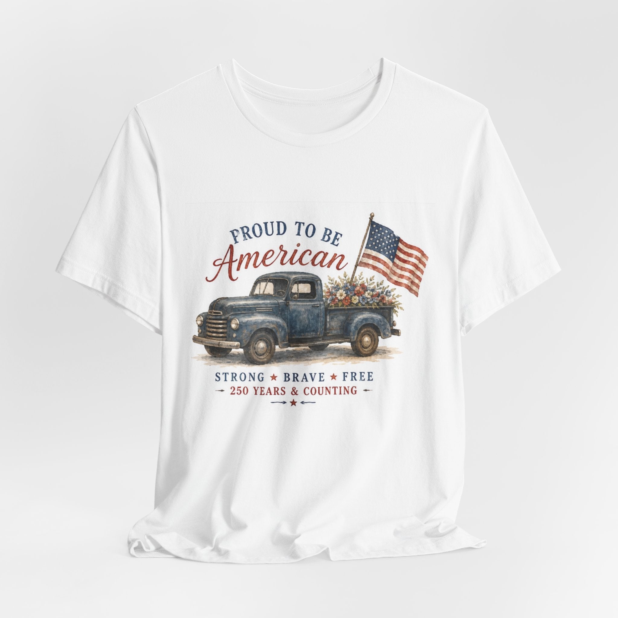 White t-shirt featuring vintage blue truck with American flag and flowers, text "Proud to Be American".
